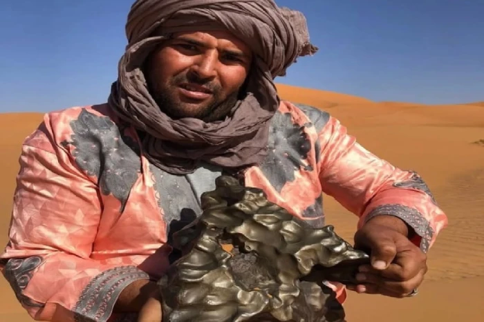 صور متداولة ل "مغربي" يحمل نيزكًا حديديًا عُثر عليه في منطقة صحراوية